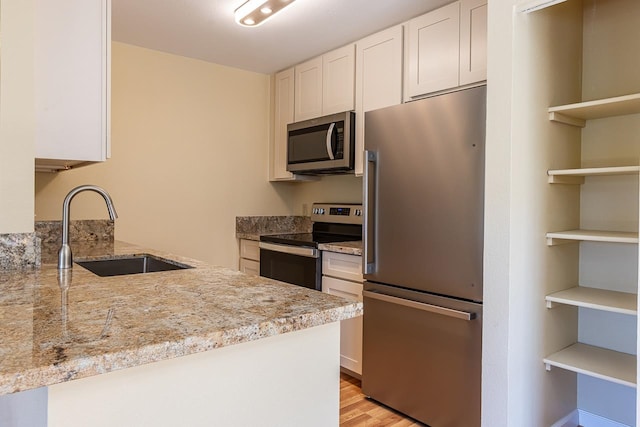 kitchen with light stone countertops, appliances with stainless steel finishes, sink, white cabinets, and light hardwood / wood-style flooring