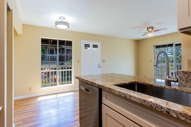 kitchen with light wood finished floors, a sink, a ceiling fan, light stone counters, and stainless steel dishwasher