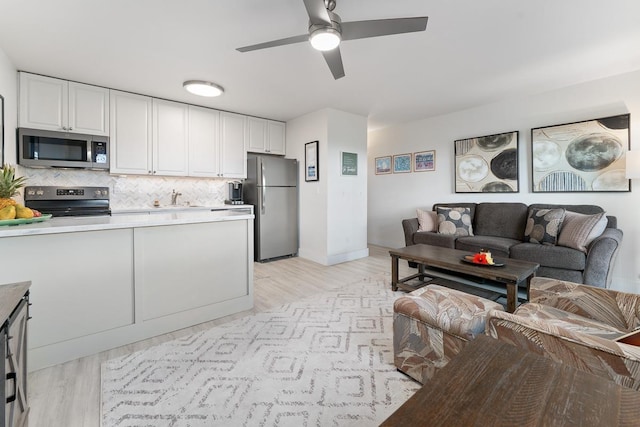 kitchen featuring white cabinets, a sink, ceiling fan, stainless steel appliances, and open floor plan