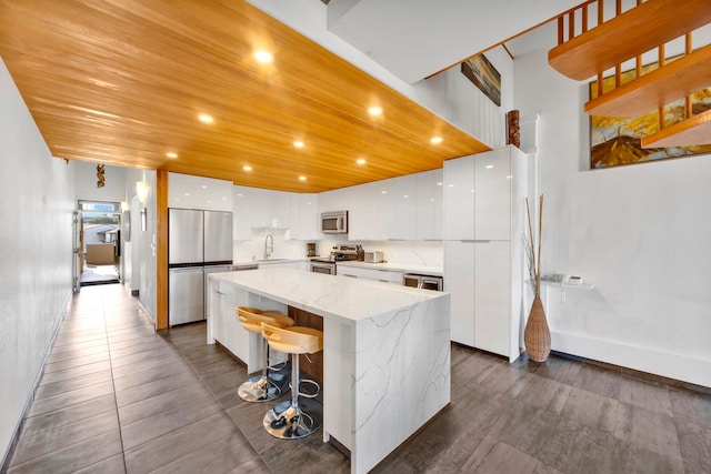 kitchen featuring white cabinets, appliances with stainless steel finishes, a center island, sink, and a breakfast bar area