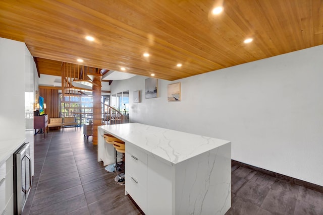 kitchen featuring wine cooler, a center island, light stone countertops, wood ceiling, and white cabinets