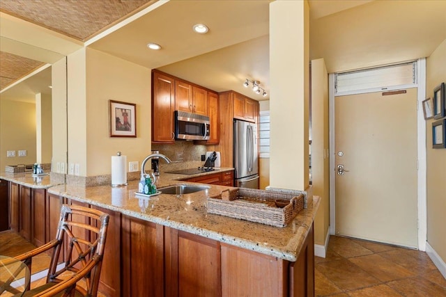 kitchen with kitchen peninsula, appliances with stainless steel finishes, light stone counters, sink, and a breakfast bar area