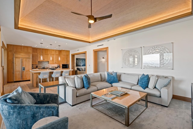 living room with wooden ceiling, a raised ceiling, a ceiling fan, and baseboards