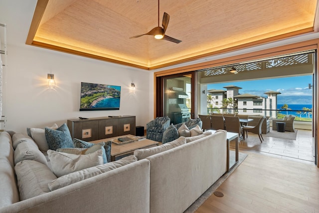 living room with a ceiling fan, a tray ceiling, wood ceiling, and light wood-style flooring