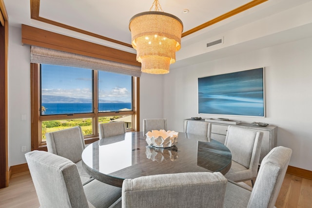 dining space featuring visible vents, baseboards, light wood-style flooring, a water view, and a chandelier