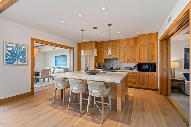 kitchen with decorative light fixtures, light countertops, backsplash, a kitchen island with sink, and black microwave