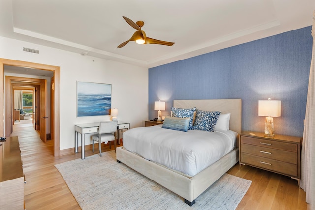 bedroom featuring light wood-style floors, baseboards, visible vents, and a tray ceiling