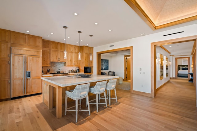 kitchen featuring hanging light fixtures, decorative backsplash, light wood-style floors, paneled refrigerator, and a kitchen breakfast bar