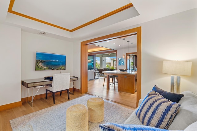 living area with light wood-type flooring, a tray ceiling, and baseboards