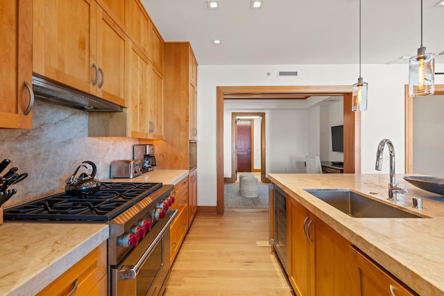 kitchen with visible vents, high end range, under cabinet range hood, pendant lighting, and a sink