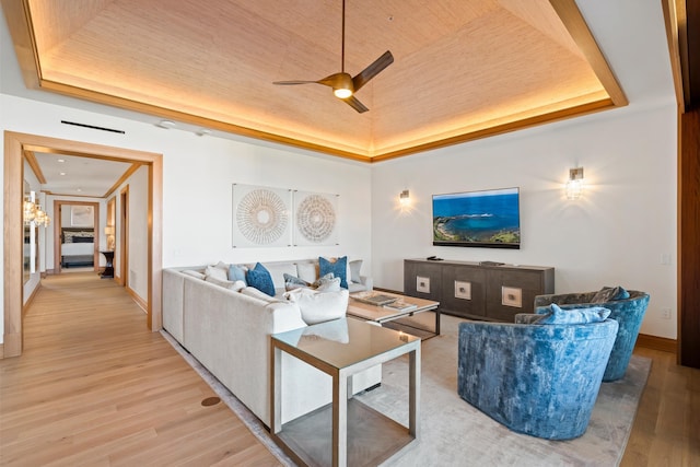 living area featuring a tray ceiling, light wood-style flooring, a ceiling fan, wooden ceiling, and baseboards