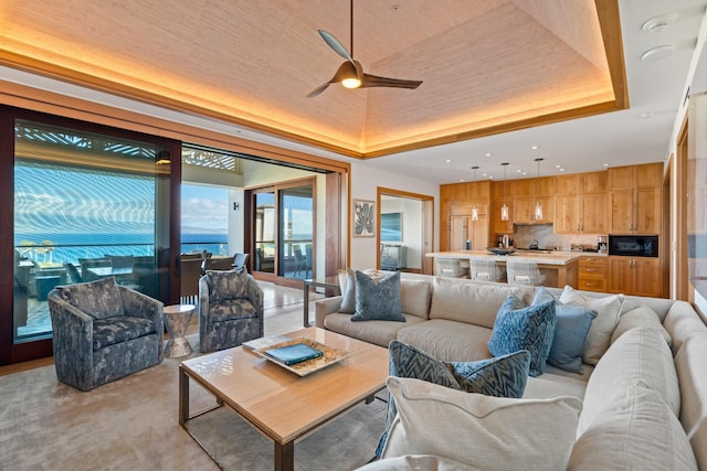 living room with ceiling fan, a raised ceiling, and light colored carpet