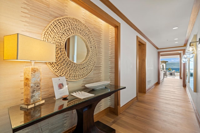 hallway with ornamental molding, wood finished floors, visible vents, and baseboards