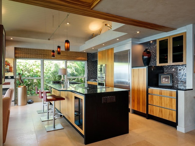 kitchen with decorative backsplash, a kitchen bar, decorative light fixtures, and a kitchen island with sink