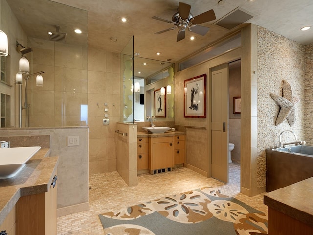 bathroom featuring vanity, ceiling fan, toilet, tiled shower, and tile walls