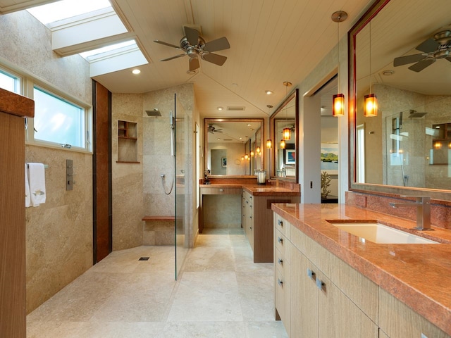 bathroom featuring ceiling fan, vanity, walk in shower, and vaulted ceiling with skylight