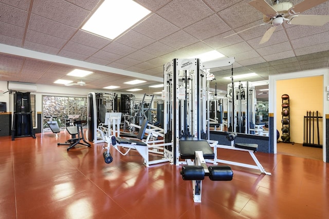 exercise room with ceiling fan, a drop ceiling, and an AC wall unit