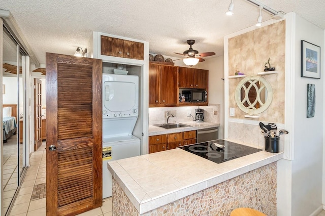 kitchen with sink, a textured ceiling, stacked washer / drying machine, light tile patterned floors, and black appliances