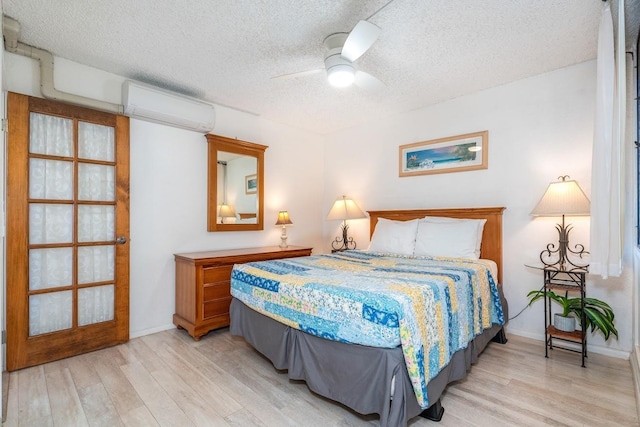 bedroom featuring ceiling fan, light hardwood / wood-style floors, a textured ceiling, and a wall mounted AC