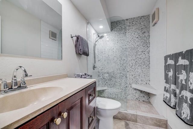 bathroom with toilet, tile walls, tiled shower, vanity, and tile patterned flooring