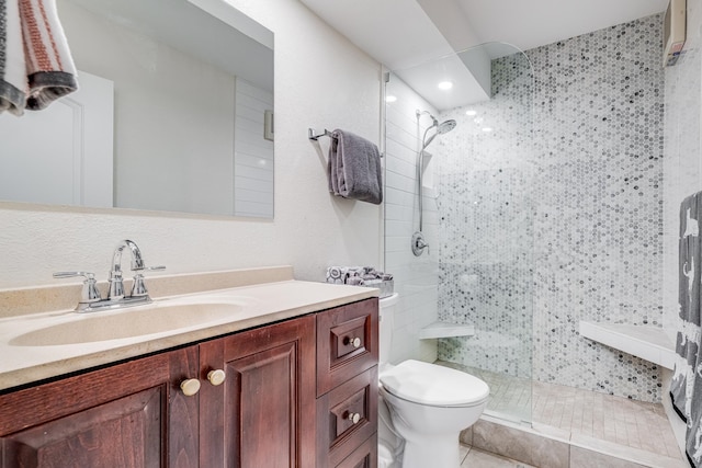 bathroom featuring vanity, a tile shower, tile patterned flooring, and toilet