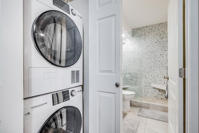 clothes washing area featuring tile walls, stacked washer / dryer, and light tile patterned floors