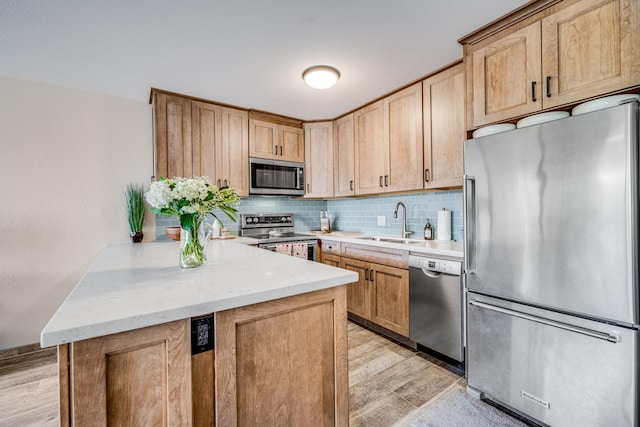 kitchen with kitchen peninsula, backsplash, sink, appliances with stainless steel finishes, and light hardwood / wood-style floors