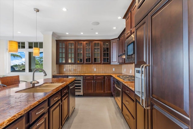 kitchen featuring pendant lighting, a sink, stone countertops, backsplash, and built in appliances