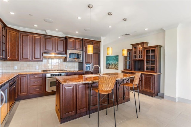 kitchen featuring built in appliances, sink, backsplash, a kitchen island with sink, and pendant lighting