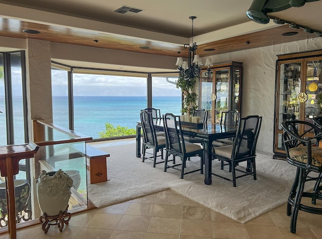 carpeted dining area with a chandelier, a raised ceiling, a water view, and a healthy amount of sunlight