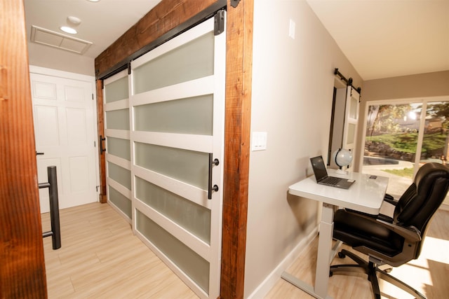 office space featuring visible vents, light wood-style flooring, baseboards, and a barn door