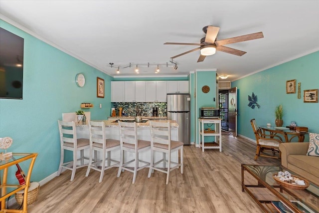 kitchen with light stone countertops, white cabinetry, tasteful backsplash, stainless steel refrigerator, and a breakfast bar area