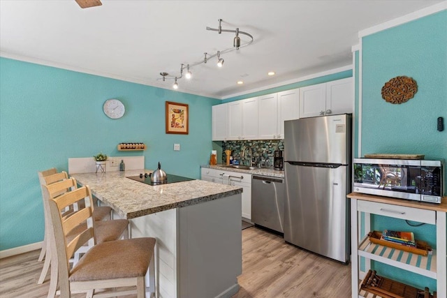 kitchen featuring a breakfast bar, kitchen peninsula, decorative backsplash, stainless steel appliances, and white cabinets