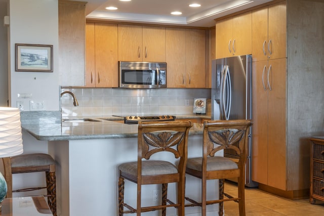 kitchen featuring sink, stainless steel appliances, a kitchen breakfast bar, decorative backsplash, and kitchen peninsula