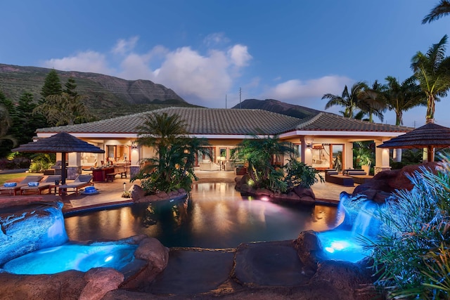 pool at dusk featuring a patio, a mountain view, and pool water feature