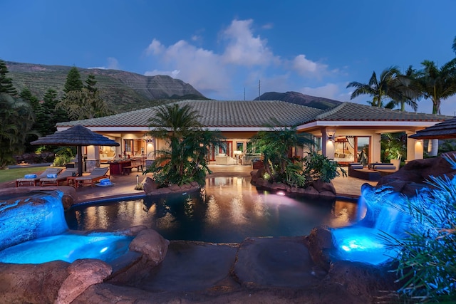 pool at dusk with a mountain view, a patio, and pool water feature