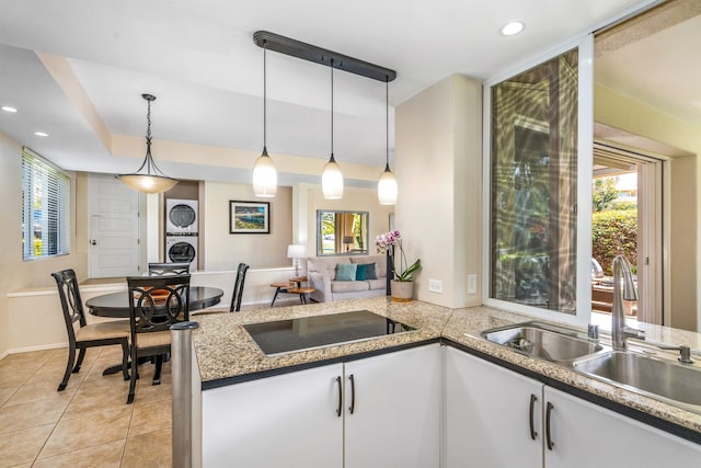 kitchen with pendant lighting, white cabinets, sink, black electric cooktop, and stacked washer and dryer