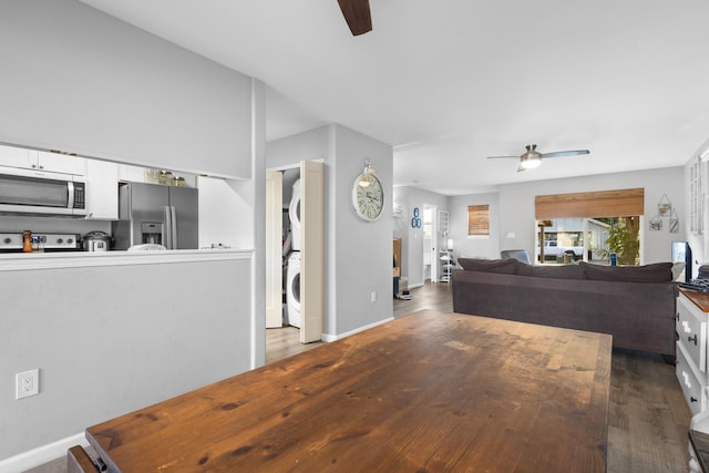 living room featuring a ceiling fan, stacked washer / dryer, baseboards, and wood finished floors