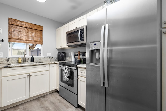 kitchen with light wood finished floors, white cabinets, light stone counters, stainless steel appliances, and a sink