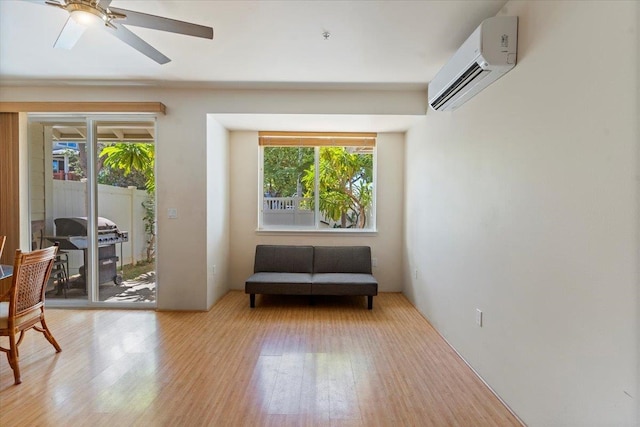 living area featuring an AC wall unit, a wealth of natural light, light hardwood / wood-style floors, and ceiling fan