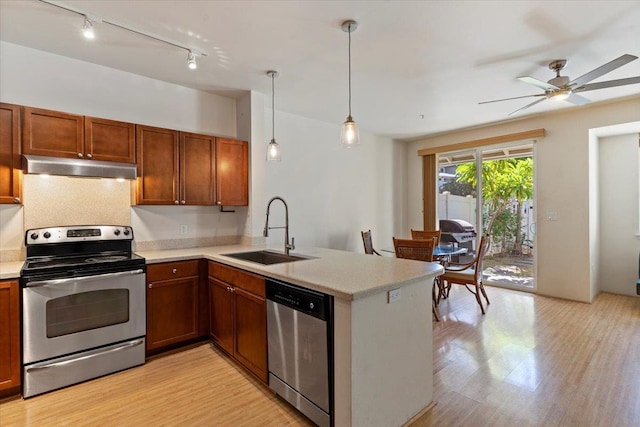 kitchen with kitchen peninsula, pendant lighting, stainless steel appliances, light wood-type flooring, and sink