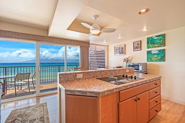 kitchen featuring ceiling fan, a center island, a water view, black electric stovetop, and light hardwood / wood-style floors