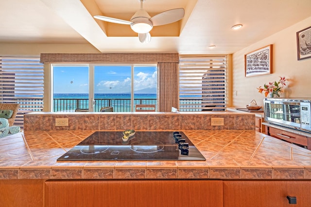 kitchen featuring a water view, black electric stovetop, tile counters, and ceiling fan