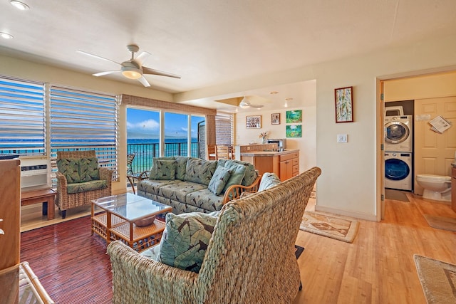 living room featuring stacked washing maching and dryer, a water view, light wood-type flooring, and ceiling fan