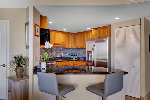 kitchen featuring dark stone countertops, tasteful backsplash, kitchen peninsula, and stainless steel refrigerator with ice dispenser