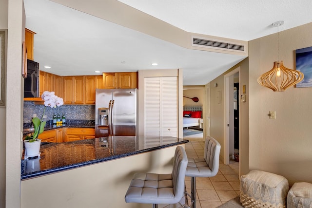 kitchen featuring hanging light fixtures, light tile patterned floors, stainless steel fridge, kitchen peninsula, and decorative backsplash