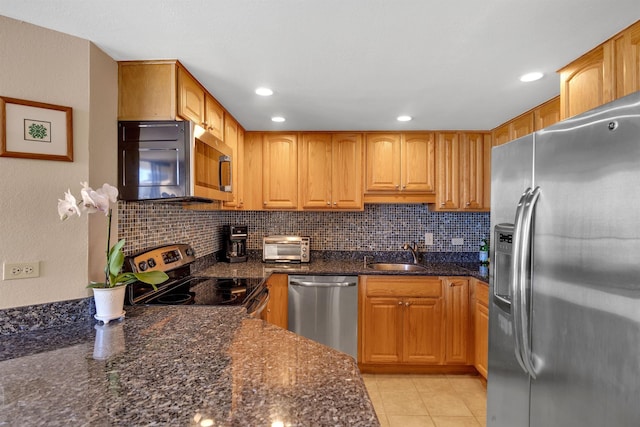 kitchen with tasteful backsplash, appliances with stainless steel finishes, sink, and dark stone counters