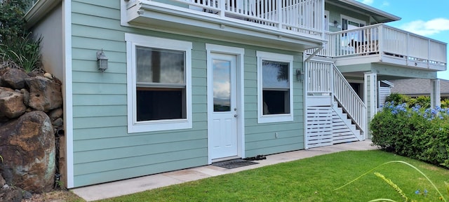 view of exterior entry featuring a balcony and a lawn