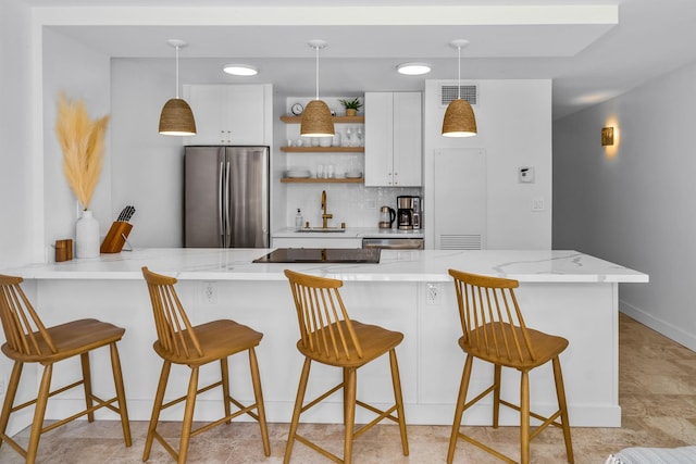 kitchen featuring a kitchen bar, stainless steel fridge, sink, decorative light fixtures, and white cabinetry