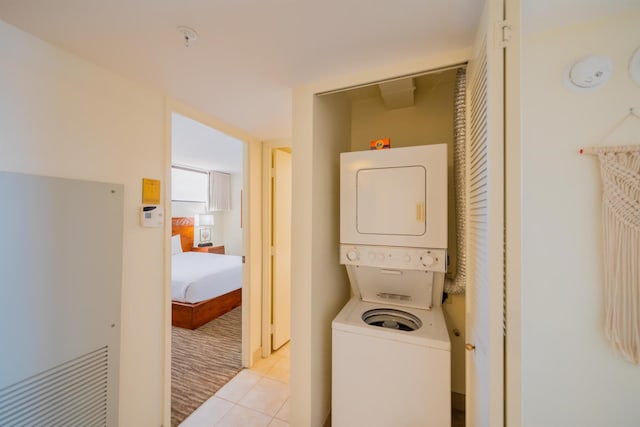 clothes washing area featuring stacked washing maching and dryer, light tile patterned floors, and laundry area